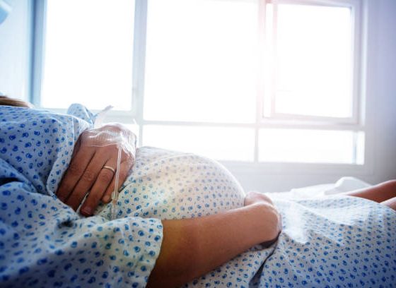 Close-up of a pregnant woman's belly in the hospital bed with catheter in hand